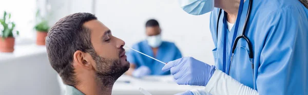 Doctor in medical mask taking samples for pcr test with nasal swab from young man, banner — Stock Photo