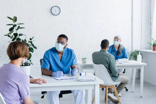 Médicos interraciales con máscaras médicas que trabajan con pacientes en un centro de vacunación - foto de stock