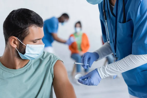 Doctor in latex gloves holding syringe near man in medical mask, vaccination concept — Stock Photo