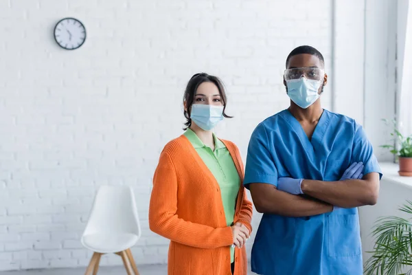 Medico afroamericano e giovane donna in maschere mediche guardando la fotocamera nel centro di vaccinazione — Foto stock