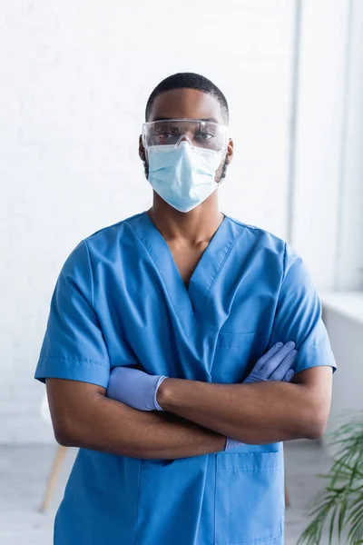 Hombre afroamericano en uniforme y máscara médica de pie con los brazos cruzados, concepto de vacunación - foto de stock