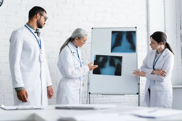 Зрілий азіатський лікар вказує на рентгенівський знімок легень на фліп-чарті поблизу молодих колег — стокове фото