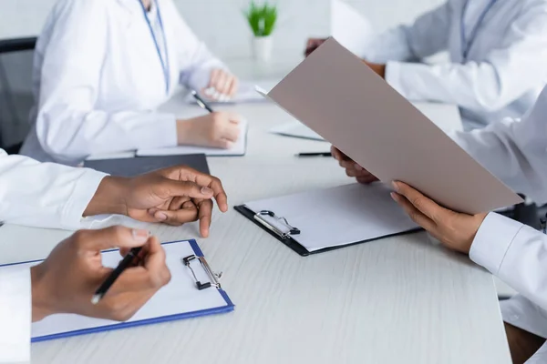 Cropped view of multiethnic doctors working with papers in conference room — Stock Photo