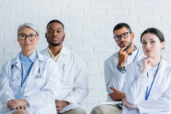 Concentrated multiethnic doctors in white coats sitting during conference — Stock Photo