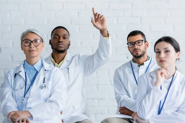 Jeune médecin afro-américain levant la main près de collègues multiethniques lors d'un séminaire médical — Photo de stock