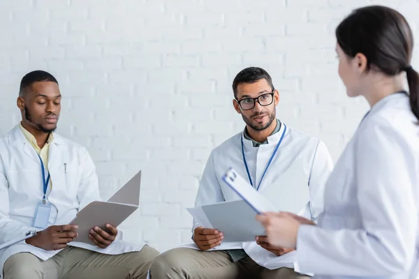 Surprised physician in eyeglasses talking to multiethnic colleagues during conference — Stock Photo