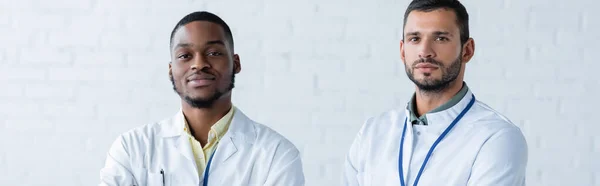 African american and european doctors in white coats looking at camera, banner — Stock Photo