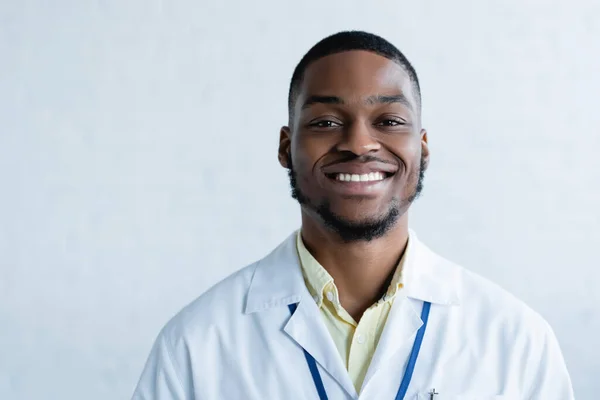 Joven y alegre afroamericano médico mirando la cámara en blanco - foto de stock