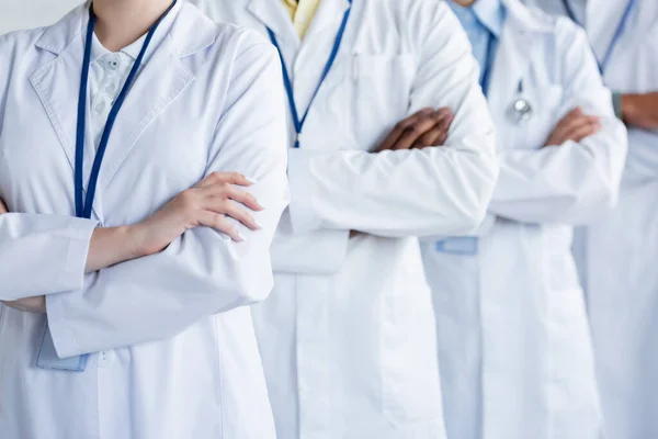 Cropped view of multicultural doctors in white coats standing with crossed arms — Stock Photo