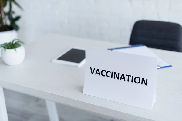 Plaque signalétique avec inscription de vaccination près de la tablette numérique floue sur le bureau de la clinique — Photo de stock