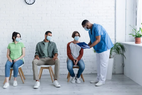 African american man standing with clipboard near patients, vaccination concept — Stock Photo