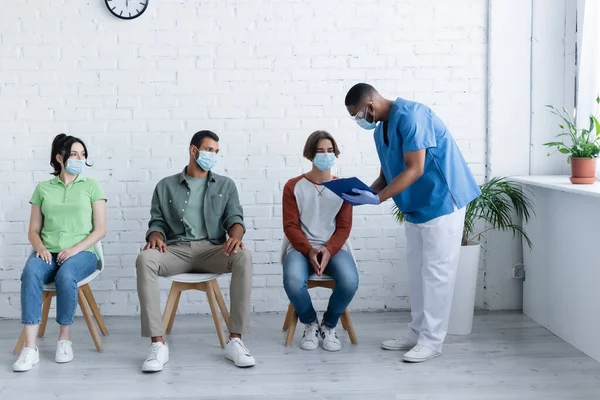 Homem americano africano de pé com prancheta perto de pacientes, conceito de vacinação — Fotografia de Stock
