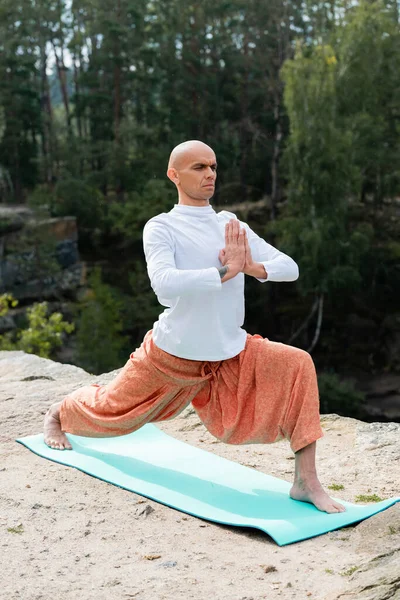 Barefoot buddhist practicing warrior pose with praying hands on rocky cliff in forest — Stock Photo