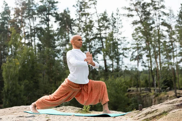 Buddhist en pantalones harem practicando yoga en pose guerrera al aire libre - foto de stock
