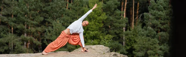 Full length view of buddhist practicing side lunge pose on rock in forest, banner — Stock Photo