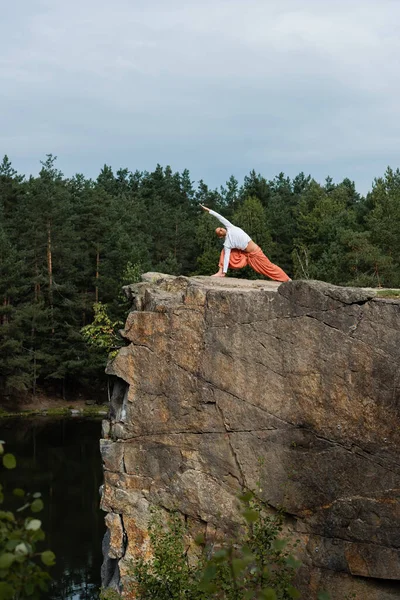 Buddhist praticando postura lunge lateral em alta penhasco rochoso sobre o rio — Fotografia de Stock