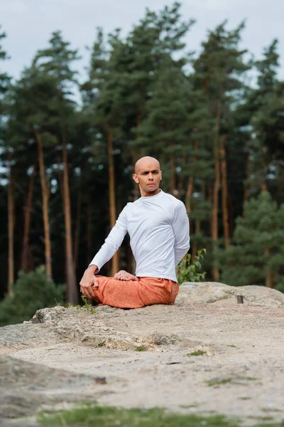 Buddhist in weißem Sweatshirt schaut weg, während er auf felsigen Klippen Lotus-Posen übt — Stockfoto