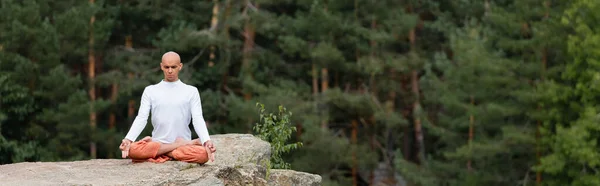 Buddhist in white sweatshirt practicing lotus pose on rock in forest, banner — Stock Photo