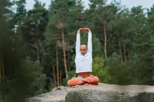 Buddhist meditando en yoga posan con las manos levantadas al aire libre en primer plano borroso - foto de stock
