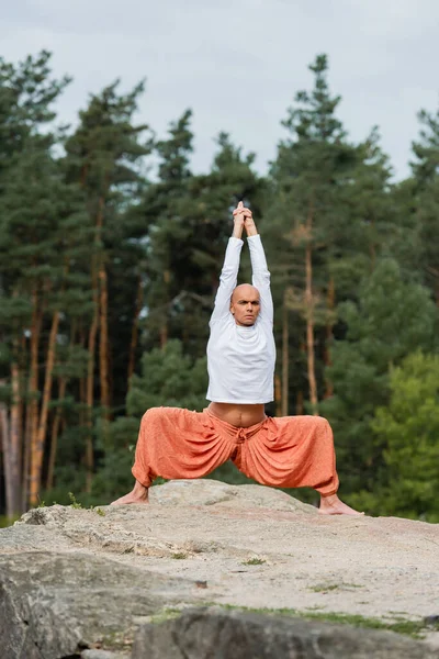 Buddhist in Sweatshirt und Haremshose meditiert in Göttin-Pose mit erhobenen Händen — Stockfoto