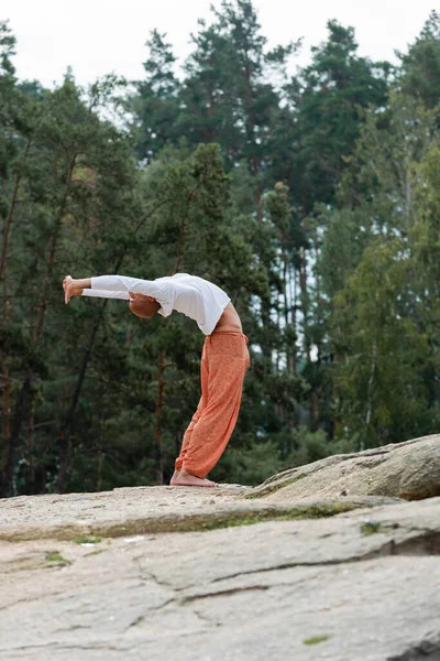Visão de comprimento total do budista meditando em pose de curva para trás na floresta — Fotografia de Stock
