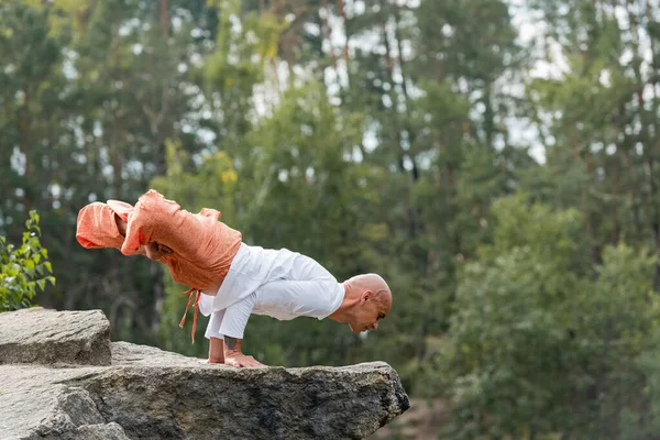 Side view of buddhist in harem pants meditating in lifted lotus pose on rocky cliff — Stock Photo