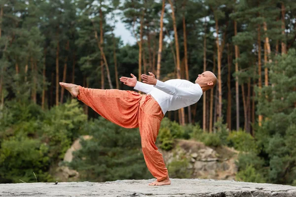 Barefoot buddhist practicing one legged backward bend pose outdoors — Stock Photo