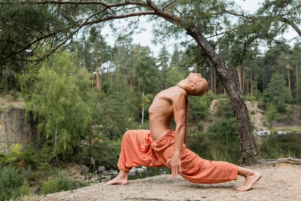 Side view of shirtless buddhist meditating in forward lunge pose outdoors — Stock Photo