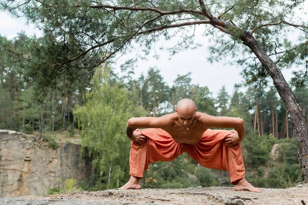 Shirtless buddhist in harem pants practicing goddess pose in forest — Stock Photo