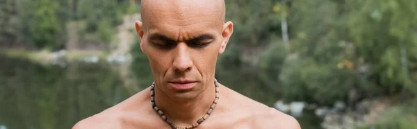 Buddhist sin camisa en cuentas meditando con los ojos cerrados al aire libre, bandera - foto de stock