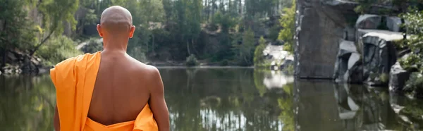 Vista trasera del monje budista meditando cerca del estanque del bosque, pancarta - foto de stock