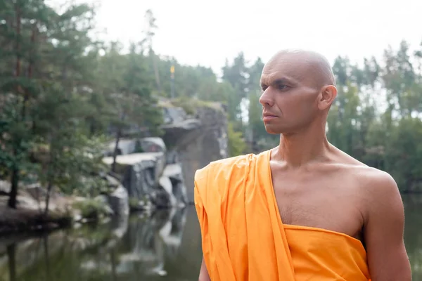 Buddhist monk in orange kasaya looking away outdoors — Stock Photo