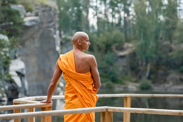 Visão traseira do budista em pé perto de cerca de madeira na floresta e olhando para longe — Fotografia de Stock