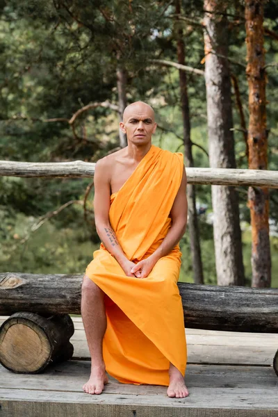 Barfüßiger Mann in buddhistischem traditionellen Gewand sitzt auf Holzbank im Wald — Stockfoto