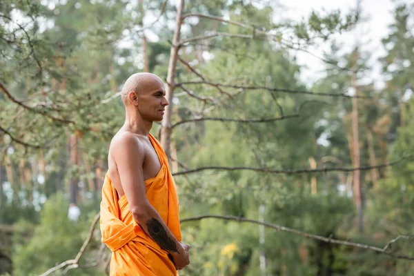 Vue latérale de l'homme tatoué en robe traditionnelle bouddhiste méditant en forêt — Photo de stock