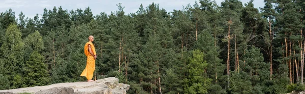 Ganzkörperansicht des Buddhisten in orangefarbenem Kasaya, der auf einem hohen Felsen meditiert, Banner — Stockfoto