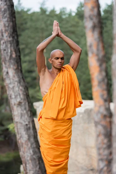 Buddhistischer Mönch mit erhobenen betenden Händen meditiert mit geschlossenen Augen im Wald — Stockfoto