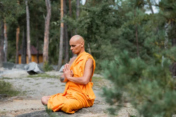 Buddhist monk in orange robe meditating with closed eyes in lotus pose — Stock Photo