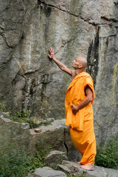 Buddhist monk in traditional orange robe touching rock — Stock Photo