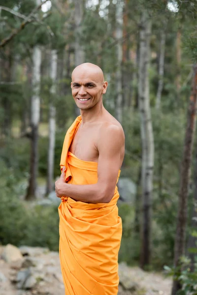 Budista feliz en naranja kasaya sonriendo a la cámara al aire libre - foto de stock