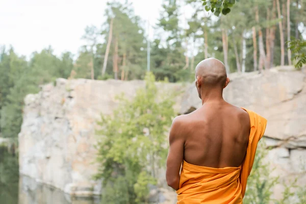 Visão traseira do homem sem pêlos em roupão budista tradicional meditando ao ar livre — Fotografia de Stock