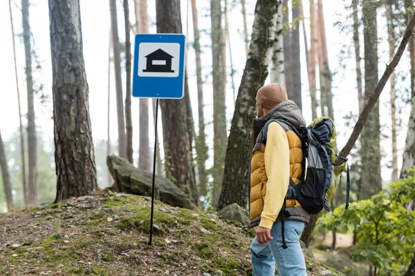 Путешественник с рюкзаком глядя на кемпинг знак в лесу — стоковое фото