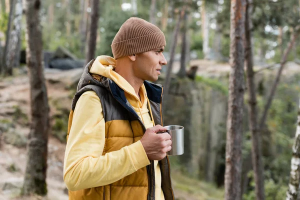 Touriste en gilet chaud et bonnet tenant tasse en métal dans la forêt — Photo de stock