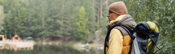 Voyageur en tenue d'automne regardant loin près de l'étang en forêt, bannière — Photo de stock