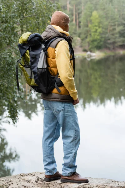 Escursionista in caldo west e jeans guardando il lago nella foresta autunnale — Foto stock