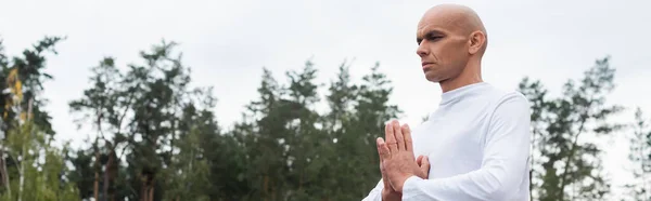 Buddhist en sudadera blanca meditando con las manos rezando al aire libre, pancarta - foto de stock