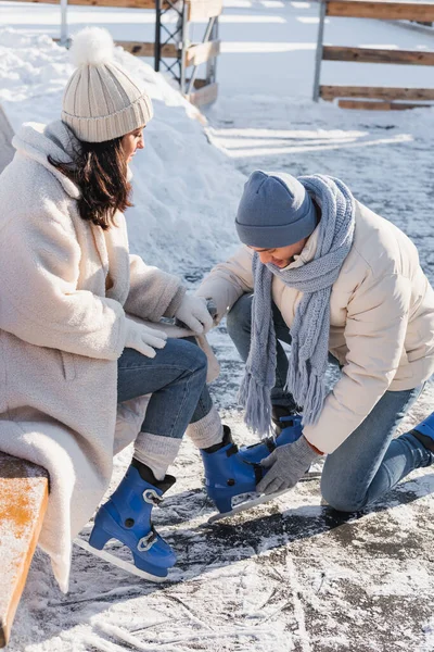 Jovem vestindo patins de gelo na bela namorada no chapéu de inverno — Fotografia de Stock