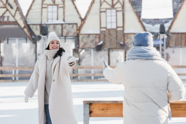 Smiling young woman in winter hat standing with outstretched hand near blurred boyfriend — Stock Photo