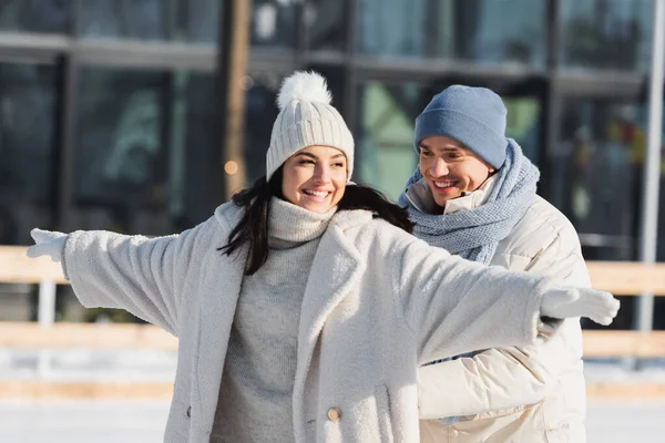 Happy young man in winter hat behind smiling girlfriend with outstretched hands — Stock Photo