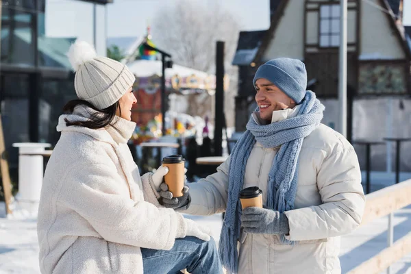 Freudiger Mann schenkt Pappbecher an glückliche Freundin mit Wintermütze — Stockfoto